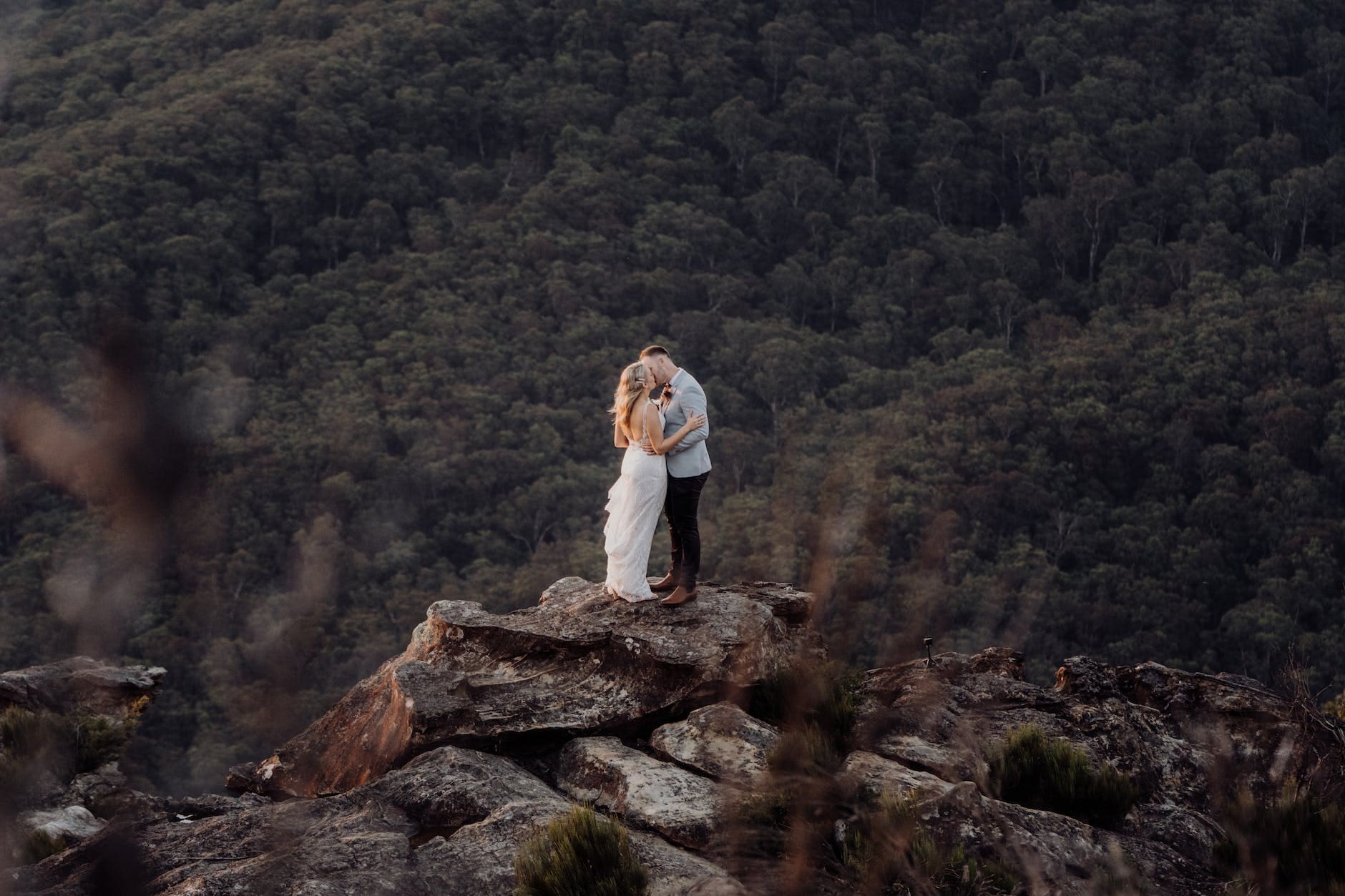 a couple standing on top of a mountain in the woods