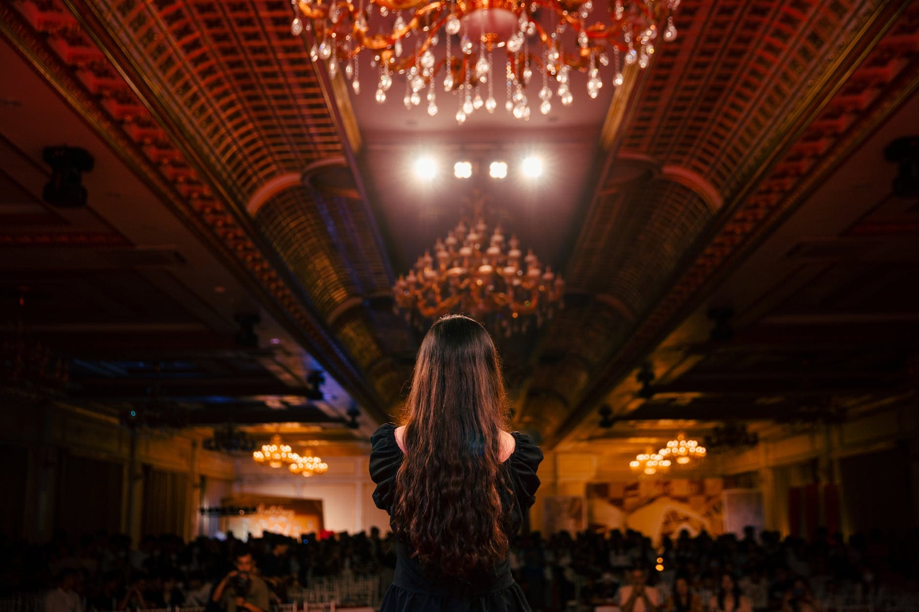 a woman standing in a large room with chandeliers