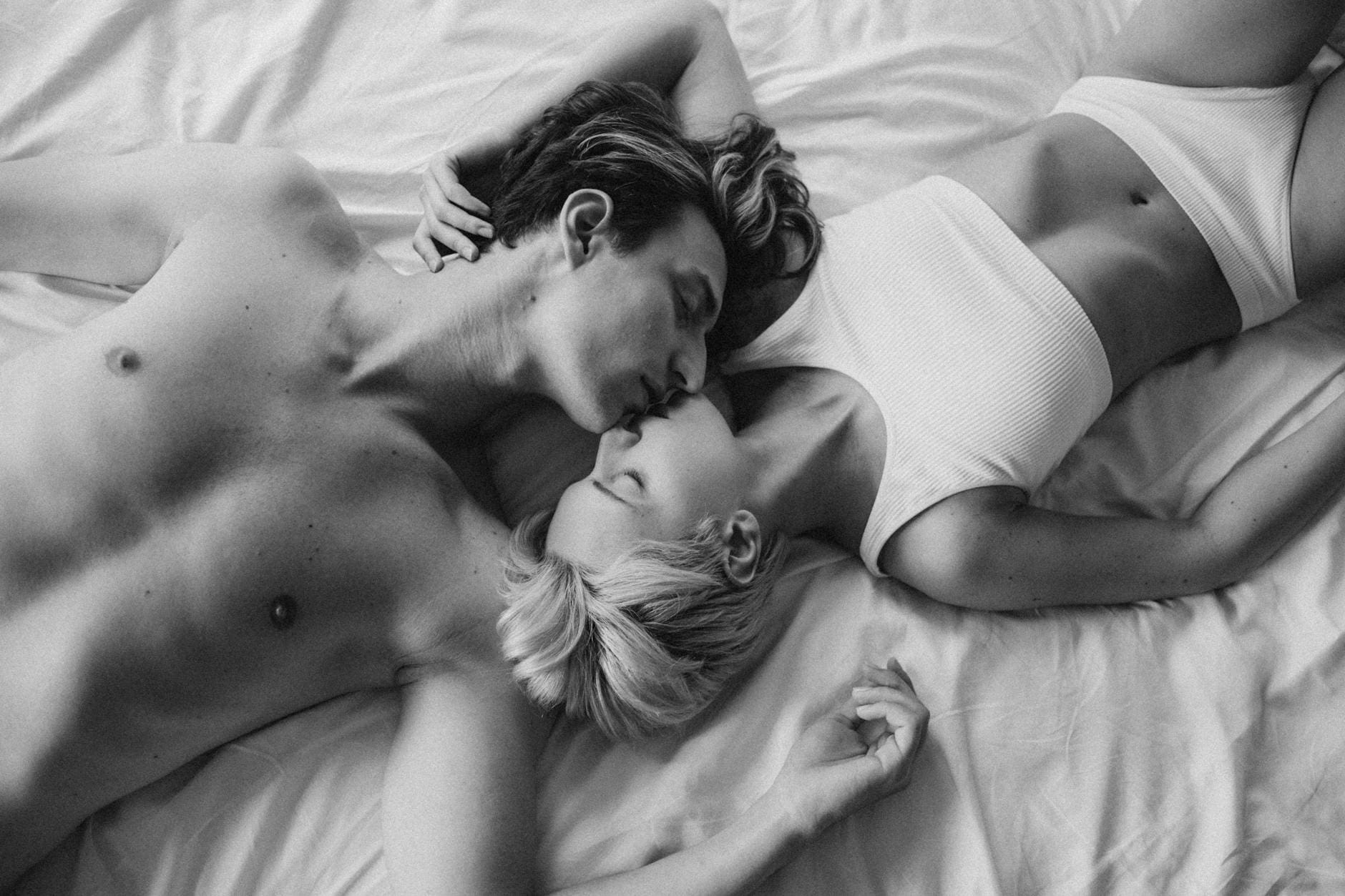 grayscale photo of a romantic couple kissing on the bed