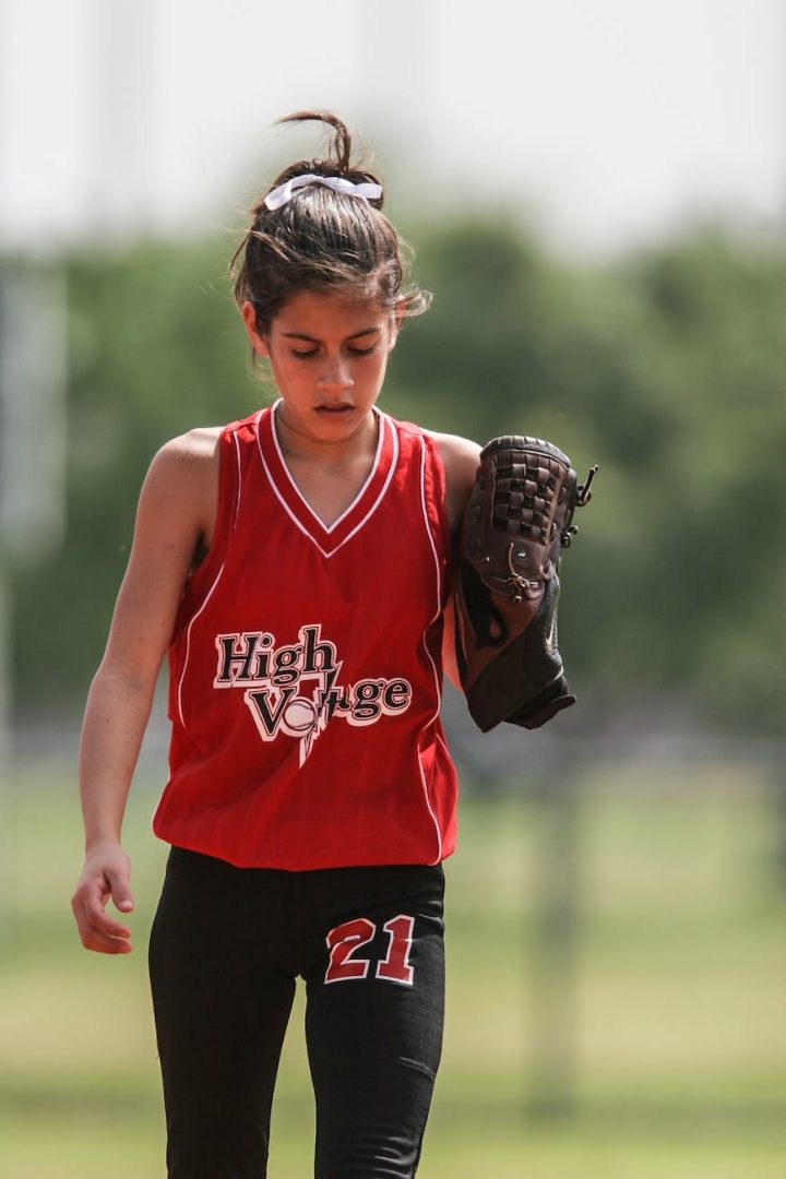 girl in red and black softball uniform walking