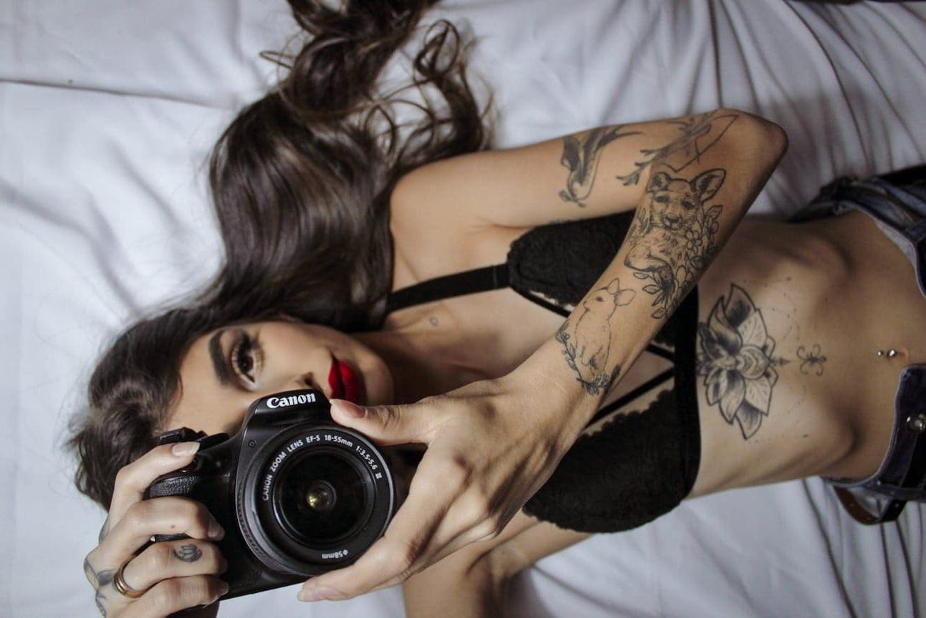 sensual woman with tattoos lying on bed with photo camera